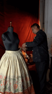 Screenshot of a Video Pin showing a man adjusting a long full skirt on a dress mold.